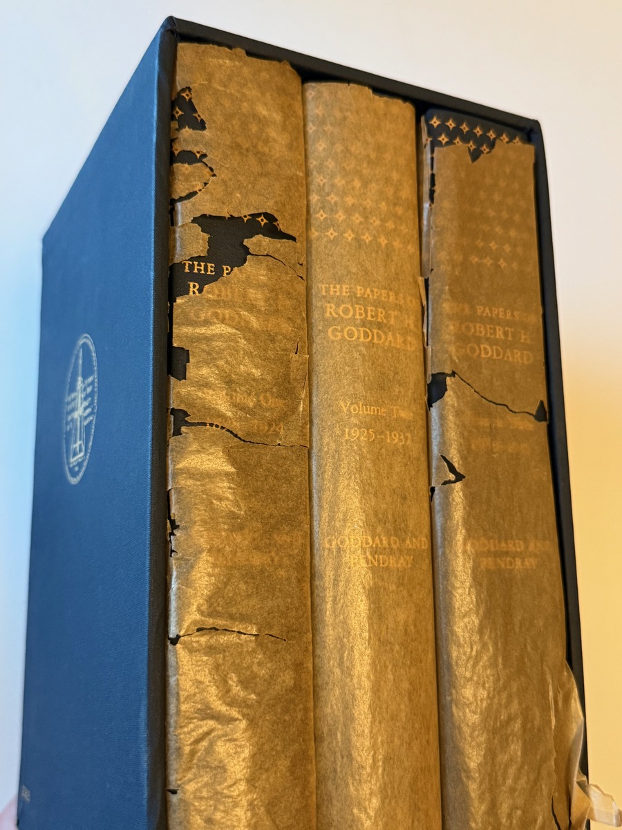 Spines of the three volumes of The Papers of Robert H. Goddard in their slipcase, showing the torn glassine wrappers
