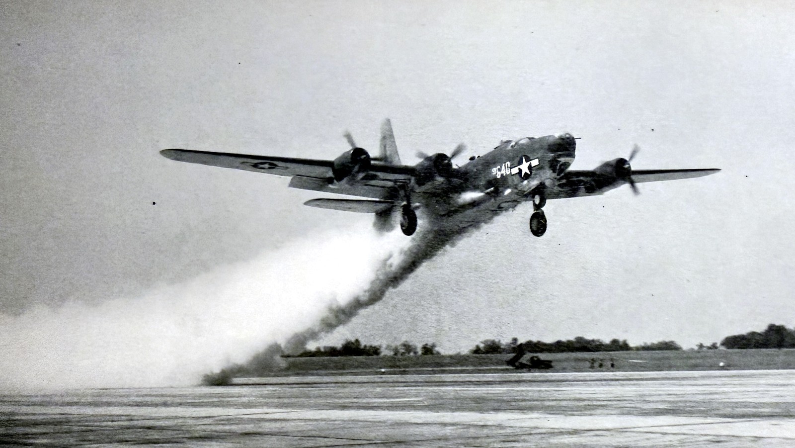 Four-engine bomber during rocket-assisted take-off, trailing a heavy smoke plume